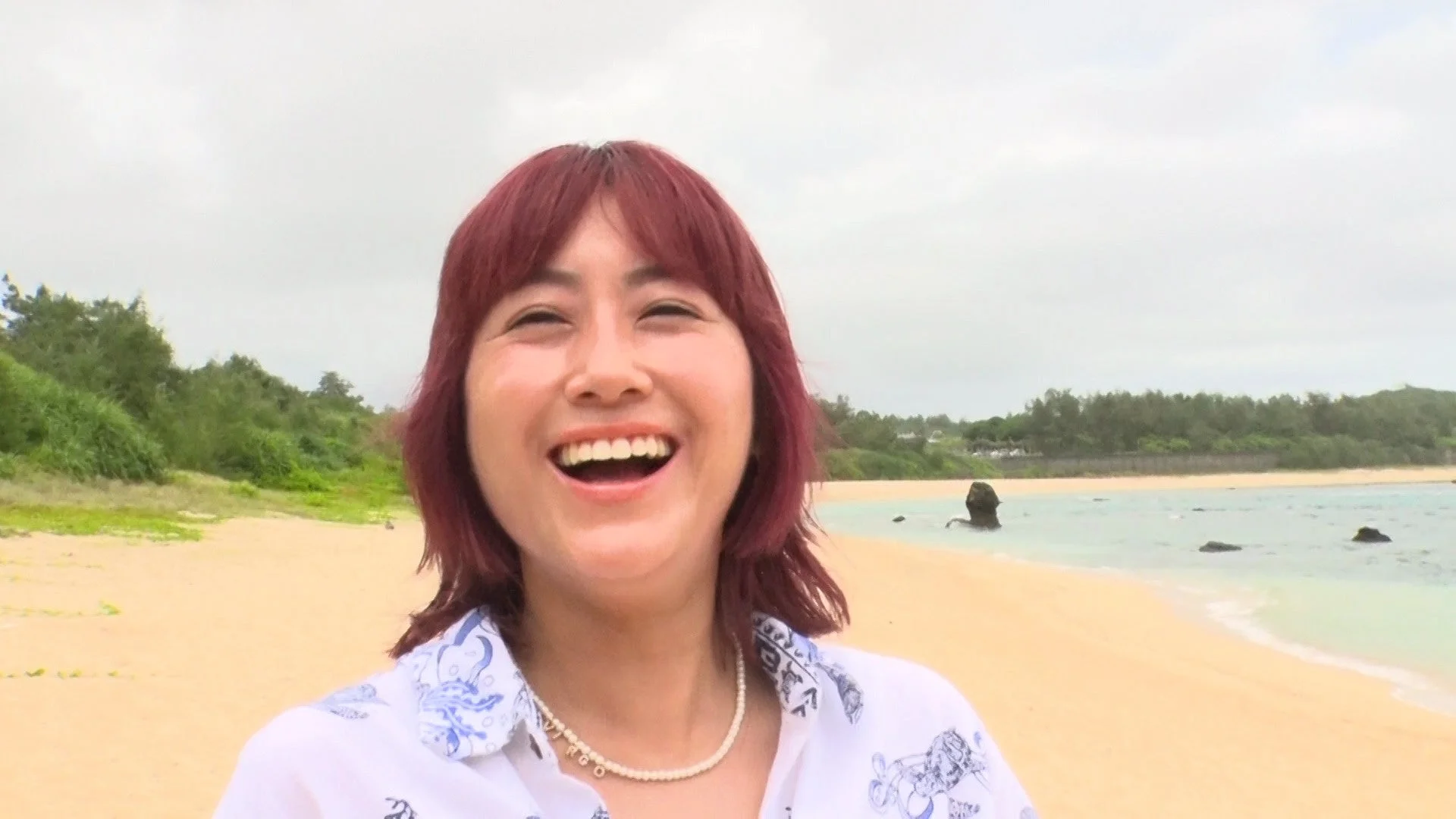 ビーチを背景に満面の笑みを浮かべるIMALUさん